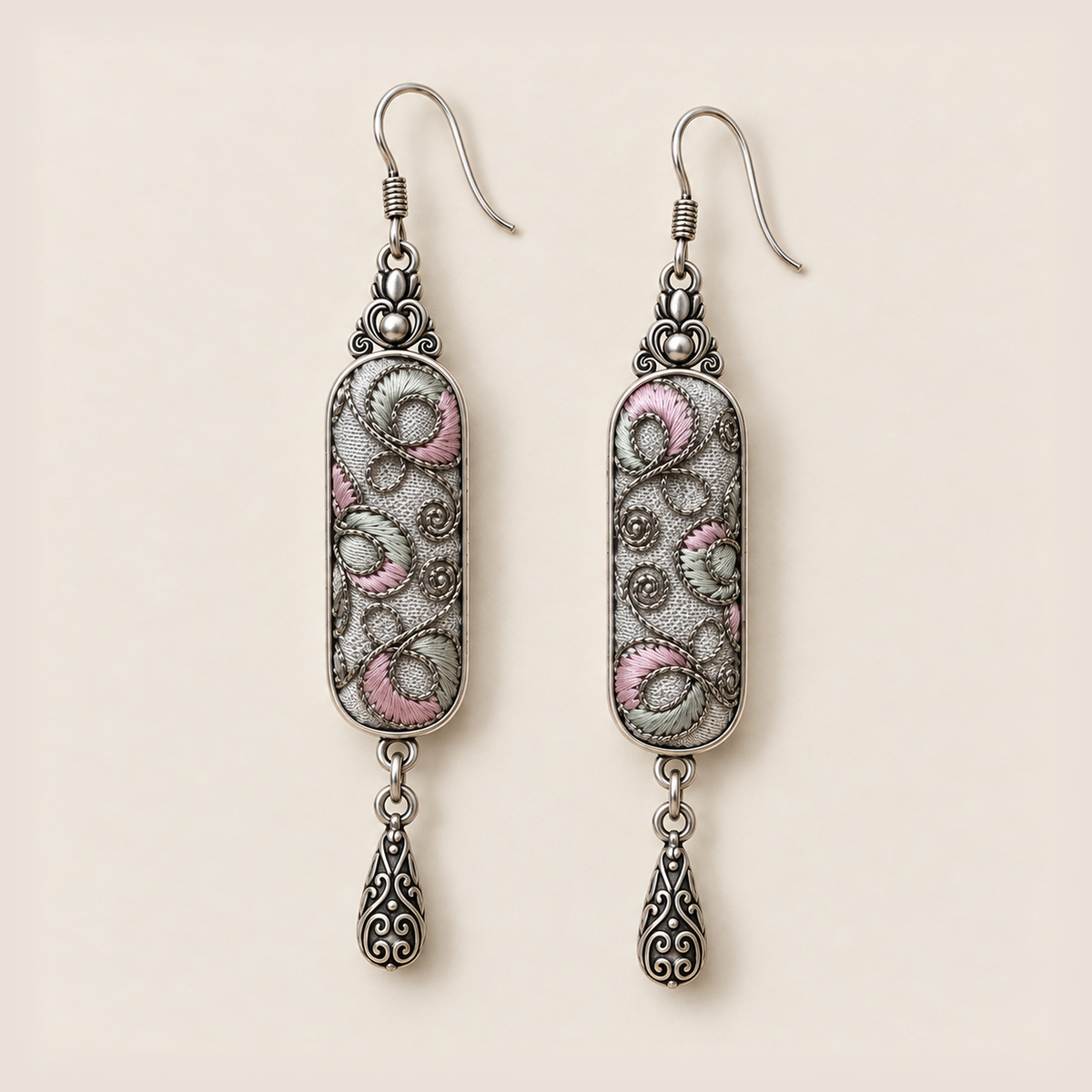 Front detail of Pastel Arabesque earrings showing different pink and green filled curves and coiled outlines on light gray textile.