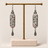 Pastel Arabesque earrings hanging from a gold-tone display stand with a pale rectangular base.