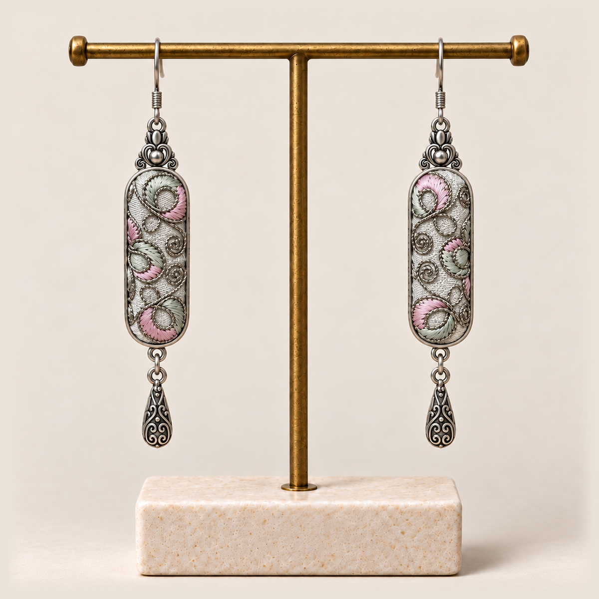 Pastel Arabesque earrings hanging from a gold-tone display stand with a pale rectangular base.