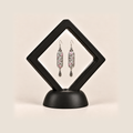 Pastel Arabesque earrings inside a black diamond-shaped display frame on a matching base.