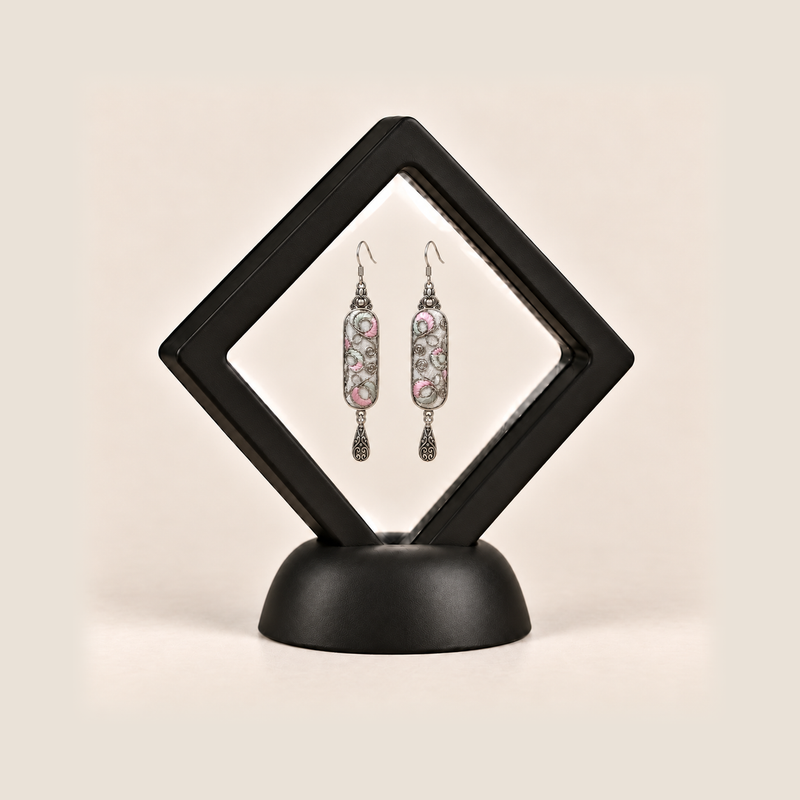 Pastel Arabesque earrings inside a black diamond-shaped display frame on a matching base.