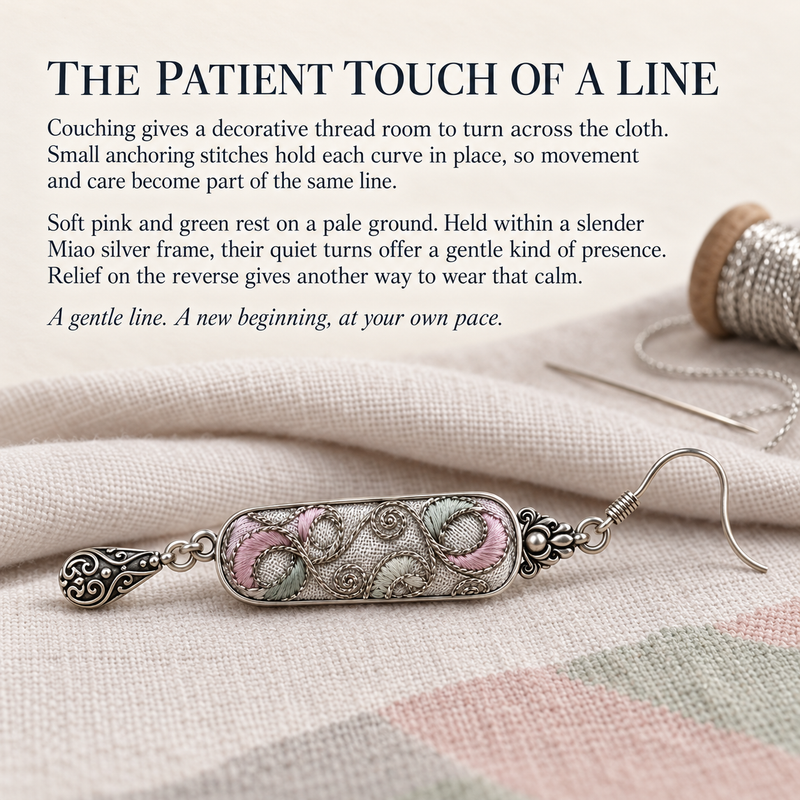Couching story card with a Pastel Arabesque earring on pale fabric beside a decorative thread spool and a needle.