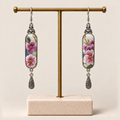 Blossom Serenade floral earrings hanging from a gold-toned display stand with a pale rectangular base.
