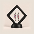 Blossom Serenade earrings displayed inside a black diamond-shaped frame on a rounded black base.