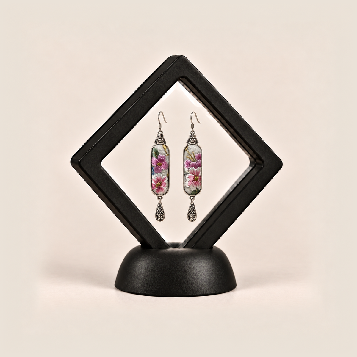 Blossom Serenade earrings displayed inside a black diamond-shaped frame on a rounded black base.