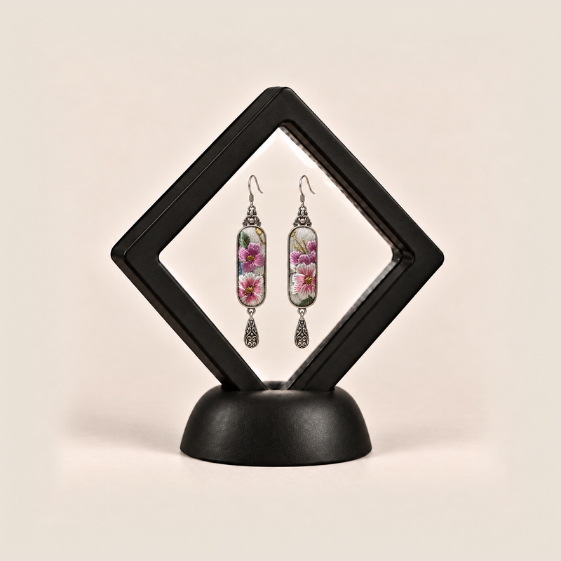 Blossom Serenade earrings displayed inside a black diamond-shaped frame on a rounded black base.