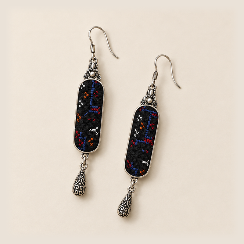 Ember Constellation earrings laid diagonally on a pale surface, showing different stitched paths across the two black panels.