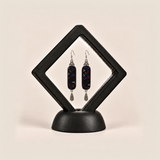Ember Constellation earrings displayed inside a black diamond-shaped frame on a rounded black base.