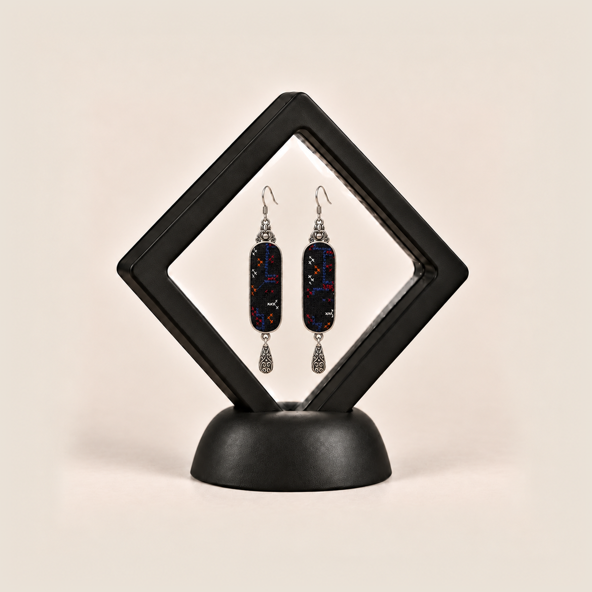Ember Constellation earrings displayed inside a black diamond-shaped frame on a rounded black base.