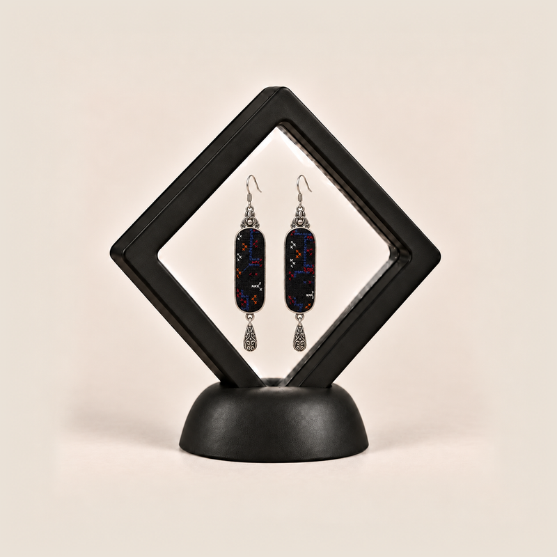 Ember Constellation earrings displayed inside a black diamond-shaped frame on a rounded black base.