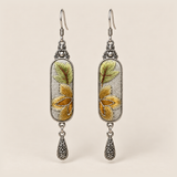 Autumn Sonata Suzhou Embroidery earrings with yellow-green leaves and ochre petals on pale gray panels, each with an engraved drop.