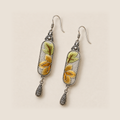 Autumn Sonata earrings laid diagonally on a pale surface, showing green leaves above ochre petals on both embroidered panels.
