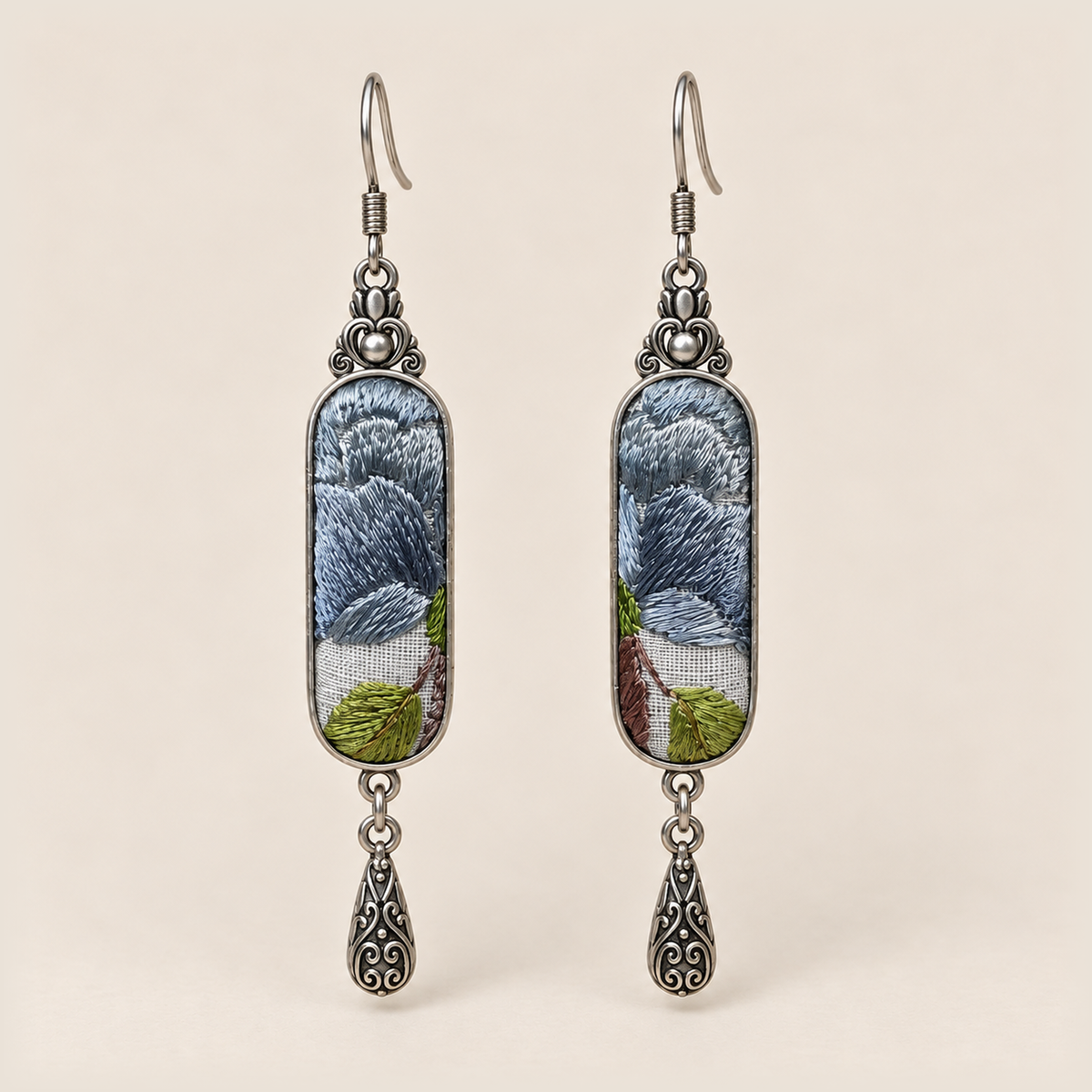 Blue Reverie Suzhou Embroidery earrings with layered blue-gray petals and green leaves on pale gray panels, each with an engraved drop.