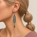 Blue Reverie earring worn with the sculpted scrollwork reverse and engraved teardrop facing outward, shown in a left-facing profile.