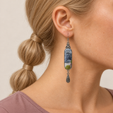 Close-up of a Blue Reverie earring with layered blue-gray petals and green leaves, worn in a right-facing profile.
