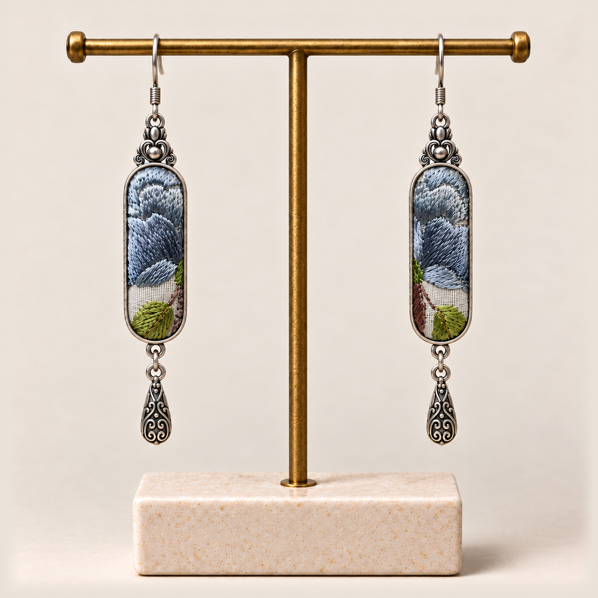 Blue Reverie earrings hanging from a gold-toned display stand with a pale rectangular base.