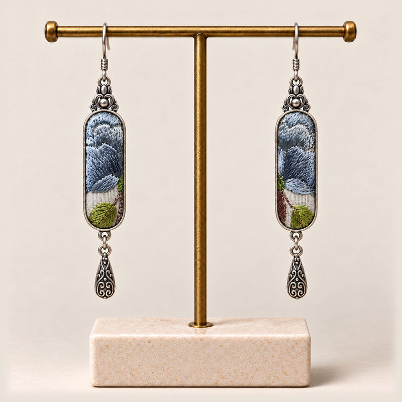 Blue Reverie earrings hanging from a gold-toned display stand with a pale rectangular base.
