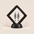 Blue Reverie earrings displayed inside a black diamond-shaped frame on a rounded black base.