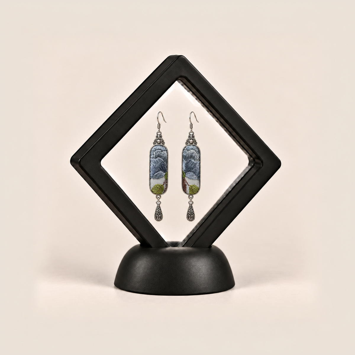 Blue Reverie earrings displayed inside a black diamond-shaped frame on a rounded black base.