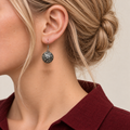 Indigo Cosmos round earring worn with the domed metal reverse and raised scrollwork facing outward.