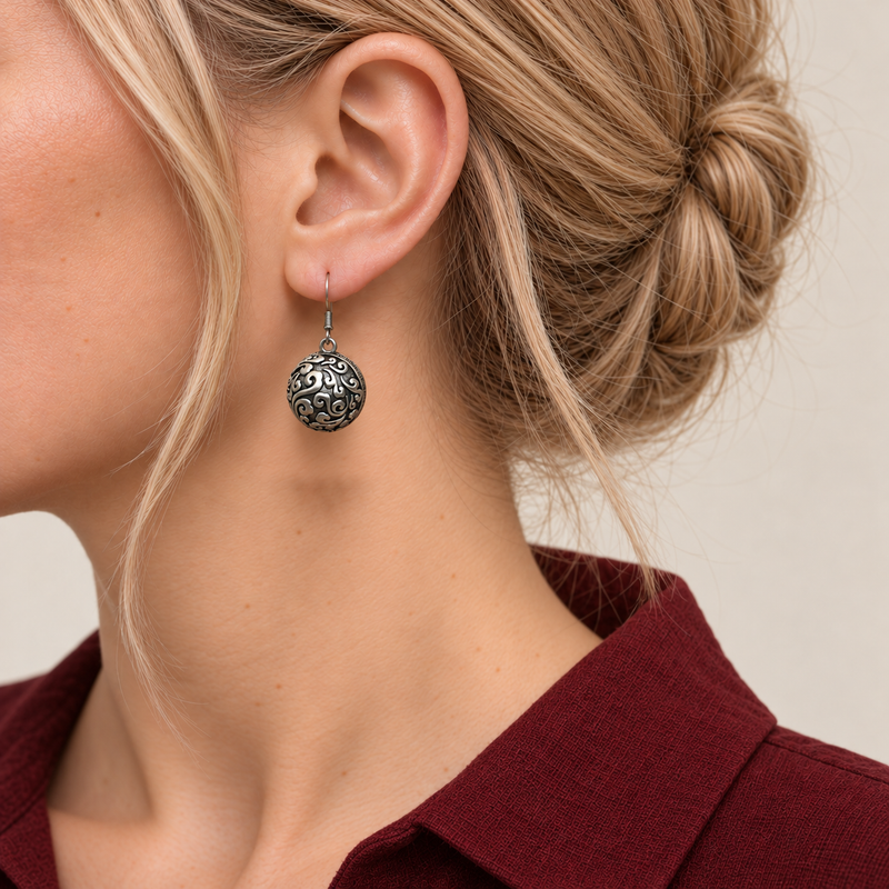 Indigo Cosmos round earring worn with the domed metal reverse and raised scrollwork facing outward.