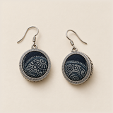 Indigo Cosmos earrings laid front-facing on a pale surface, showing different pale curved motifs within geometric circular rims.