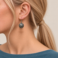 Coral Rhapsody round earring worn with its domed metal reverse and raised curling scrollwork facing outward.