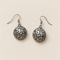 Coral Rhapsody earrings laid back-facing on a pale surface, showing rounded metal backs covered in raised scrollwork.