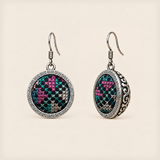Petal Mosaic round earrings with pink, teal and pale counted-thread embroidery on dark fabric, geometric rims and domed backs.