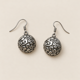 Verdant Bloom earrings laid back-facing on a pale surface, showing domed metal backs with raised curling patterns.