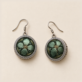 Verdant Bloom earrings laid front-facing, showing shaded green petals on dark green fabric within geometric circular rims.