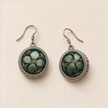 Verdant Bloom earrings laid front-facing, showing shaded green petals on dark green fabric within geometric circular rims.