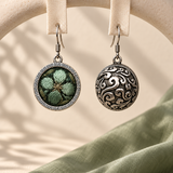 Verdant Bloom earrings hanging from pale woven fabric strips, showing the green floral front and domed scrollwork reverse.