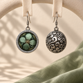 Verdant Bloom earrings hanging from pale woven fabric strips, showing the green floral front and domed scrollwork reverse.