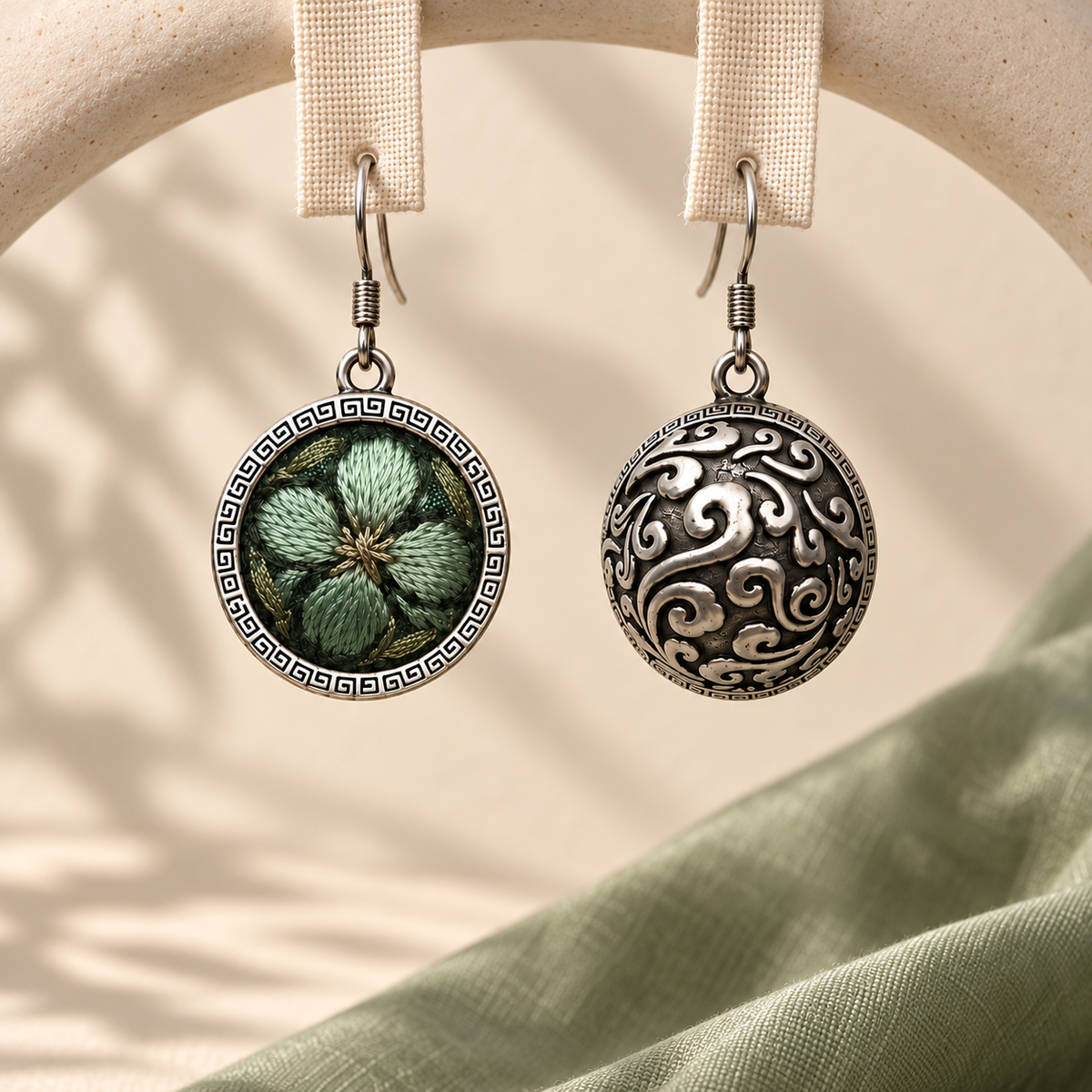 Verdant Bloom earrings hanging from pale woven fabric strips, showing the green floral front and domed scrollwork reverse.