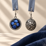Sapphire Reverie earrings hanging from blue woven fabric strips, showing the embroidered flower front and domed scrollwork reverse.