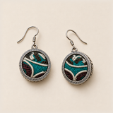 Jade Arabesque earrings laid front-facing, showing individual pale curved outlines and teal and burgundy embroidery within circular rims.