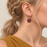 Crimson Cadence earring worn with its red embroidered front, gold-colored outlines and teal and magenta accents facing outward.