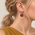 Crimson Cadence earring worn with its red embroidered front, gold-colored outlines and teal and magenta accents facing outward.