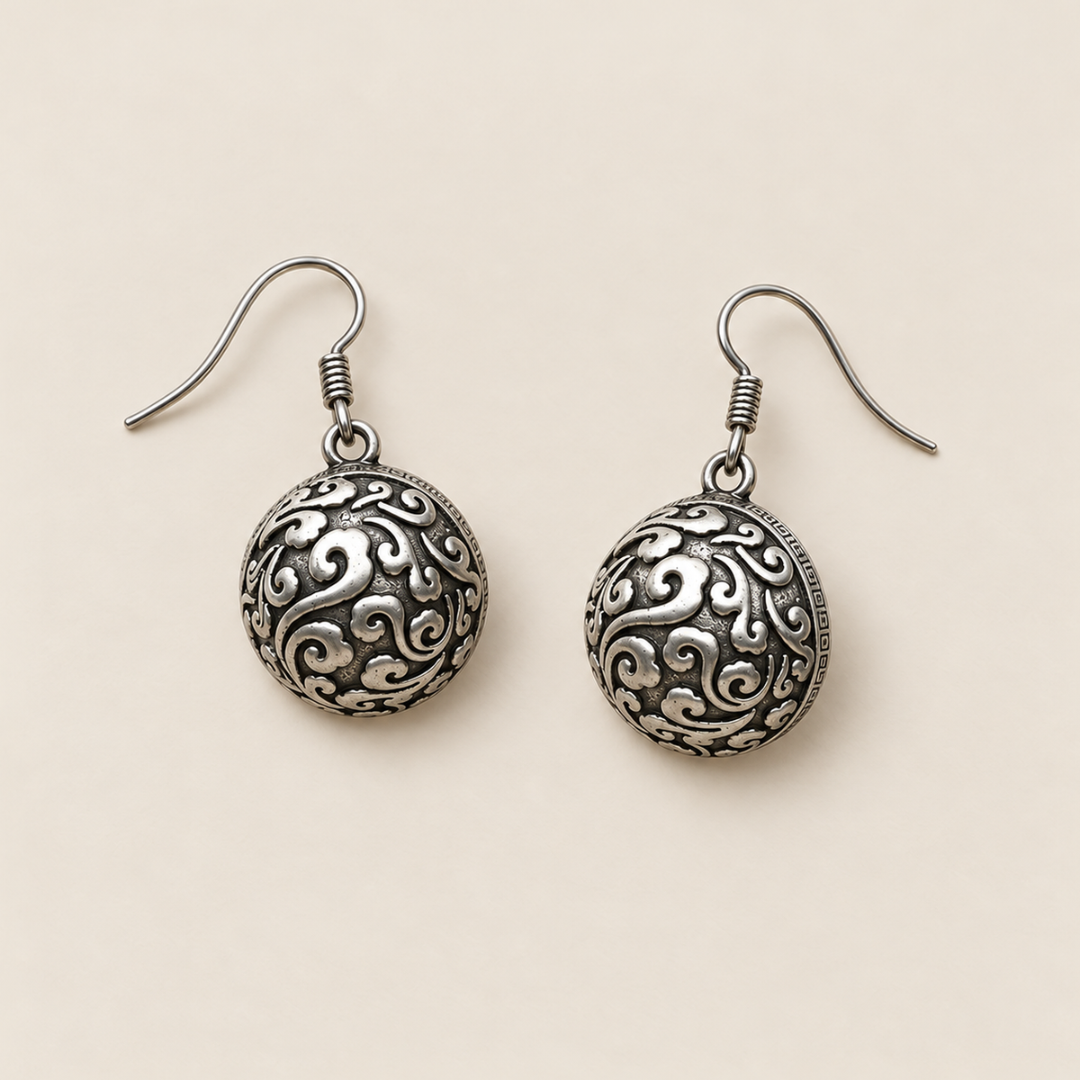Crimson Cadence earrings laid back-facing on a pale surface, showing domed metal backs with raised curling patterns.