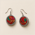 Crimson Cadence earrings laid front-facing, showing different gold-colored curves and teal and magenta accents on red embroidery.