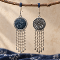 Indigo Canticle earrings hanging from blue loops on a branch, showing the batik front, floral reverse and long chain tassels.