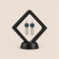 Indigo Canticle earrings displayed inside a clear membrane in a black square frame set diagonally on a black base.