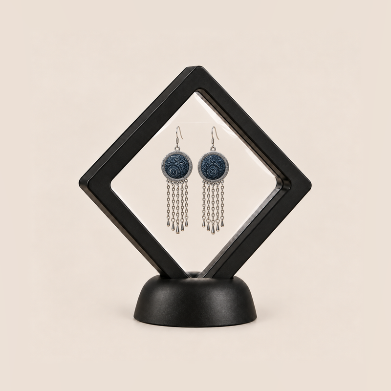 Indigo Canticle earrings displayed inside a clear membrane in a black square frame set diagonally on a black base.