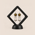 Golden Benediction earrings displayed inside a clear membrane in a black square frame set diagonally on a black base.