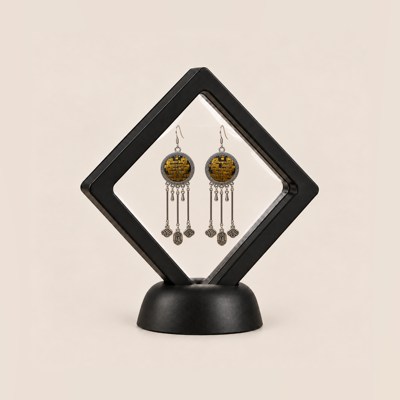Golden Benediction earrings displayed inside a clear membrane in a black square frame set diagonally on a black base.