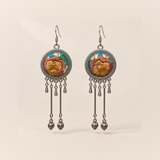 Amber Floraison earrings with ochre and rust-colored embroidered flowers on turquoise cloth, two long rods with bud pendants and three short drops.