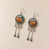 Amber Floraison earrings laid front-facing, showing individual ochre and rust-colored floral stitches, three short drops and two hanging bud pendants on each.