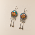 Amber Floraison earrings laid front-facing, showing individual ochre and rust-colored floral stitches, three short drops and two hanging bud pendants on each.