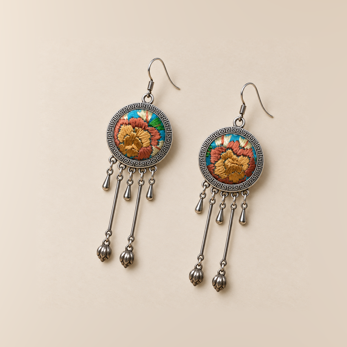 Amber Floraison earrings laid front-facing, showing individual ochre and rust-colored floral stitches, three short drops and two hanging bud pendants on each.